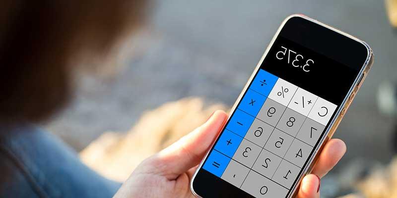 A hand holds a calculator with blue, white, and grey buttons on it. The display reads 3.375